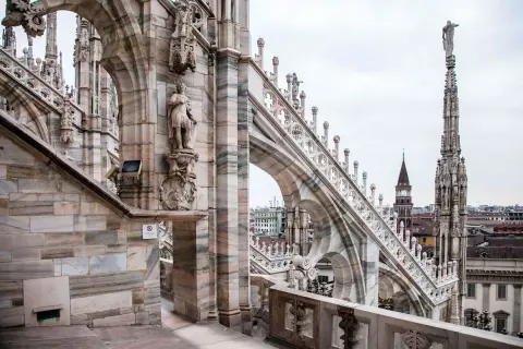 Dettaglio delle guglie e delle statue sui tetti del Duomo di Milano, con la città sullo sfondo.