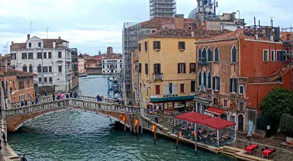 Il ponte delle Guglie attraversa un canale veneziano, circondato da edifici storici e persone che passeggiano.