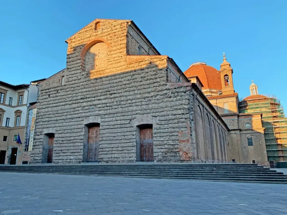 La Basilica di San Lorenzo a Firenze, con la sua facciata in pietra grezza e la cupola arancione, illuminata dal sole del tramonto.