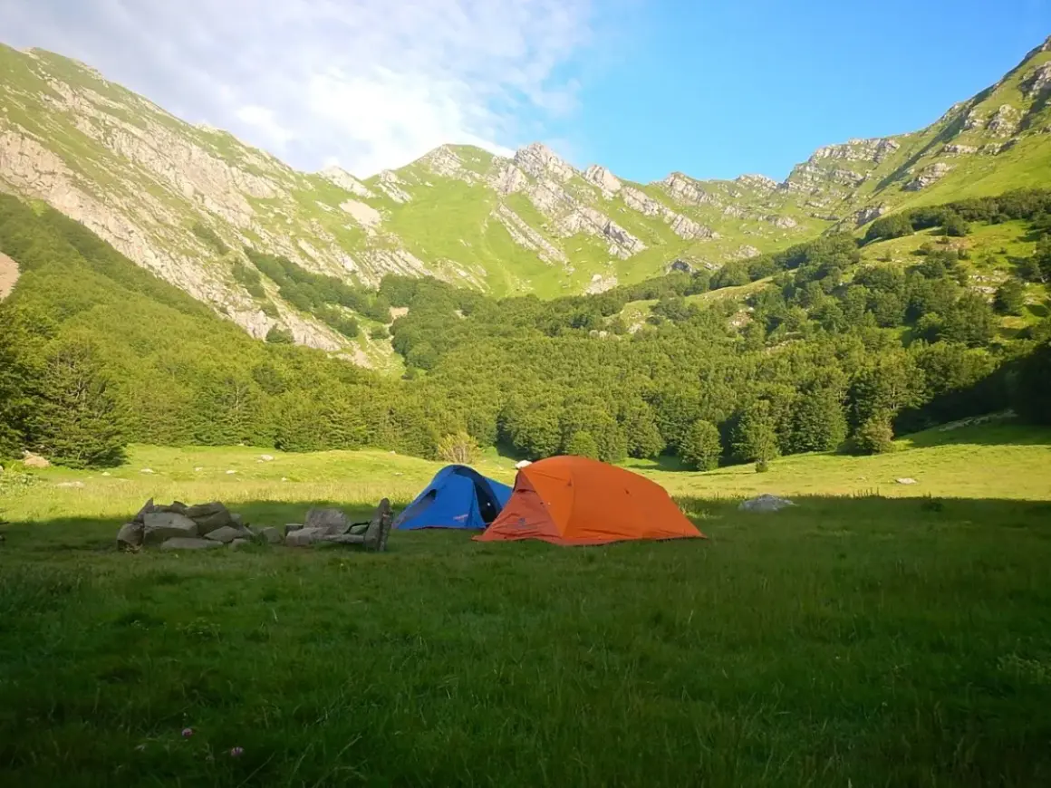 Tende da campeggio in un prato verde, con montagne boscose sullo sfondo, vicino alle sorgenti del Secchia.