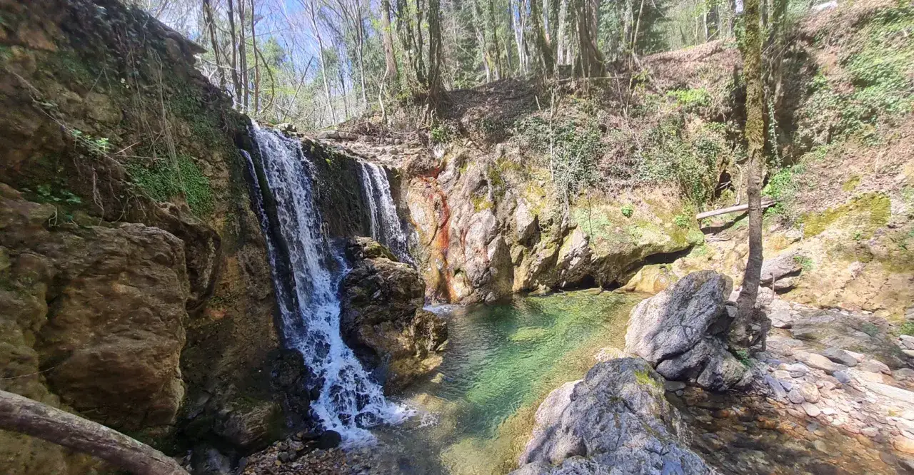 Cascata nella riserva naturale Alto Merse, con acque cristalline che scendono tra rocce e vegetazione lussureggiante.