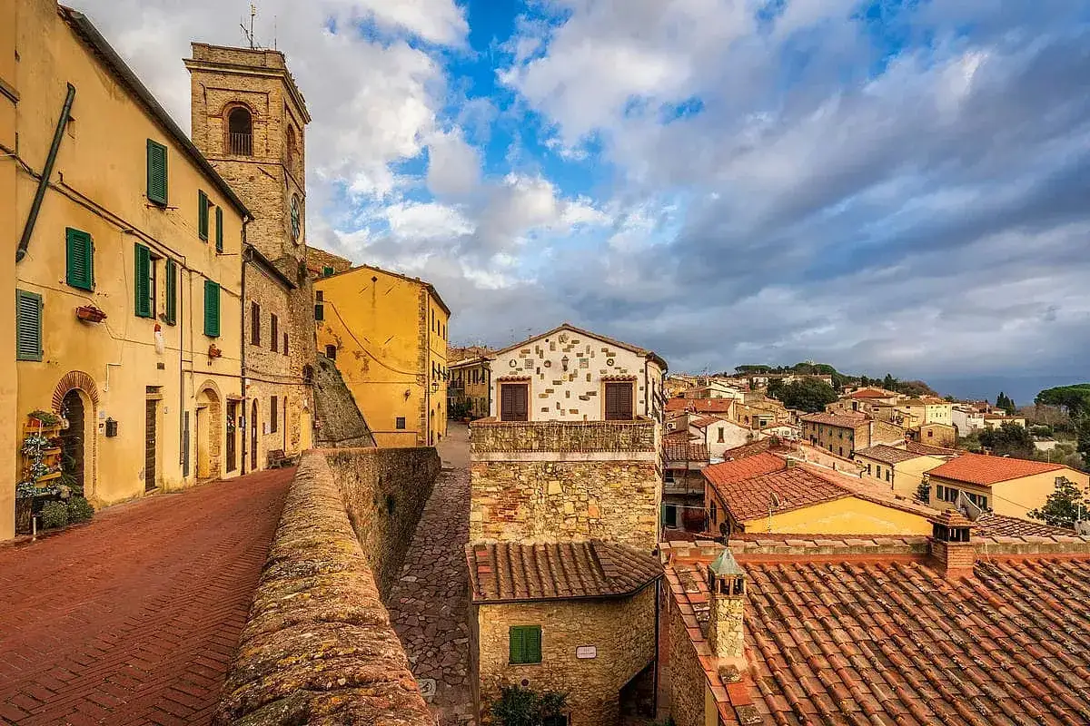 Montescudaio cosa vedere: un borgo toscano con case gialle, un campanile e tetti rossi sotto un cielo nuvoloso.