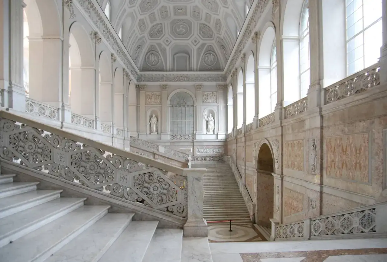 Magnifica scalinata in marmo del palazzo reale Napoli, con soffitto a volta decorato e statue classiche.