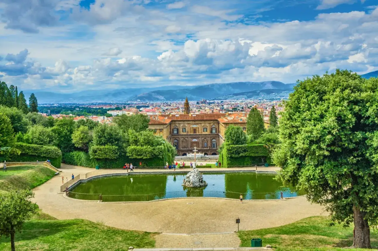 Un laghetto verde e un palazzo storico dominano la vista panoramica dei Giardini di Boboli, con Firenze sullo sfondo.