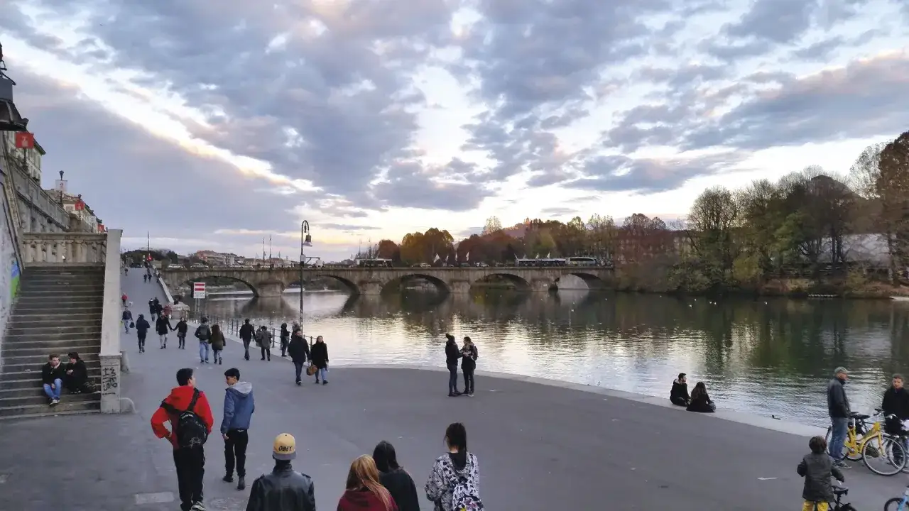 Passeggiata serale sui murazzi Torino, con gente che cammina e ammira il fiume e il ponte illuminato.