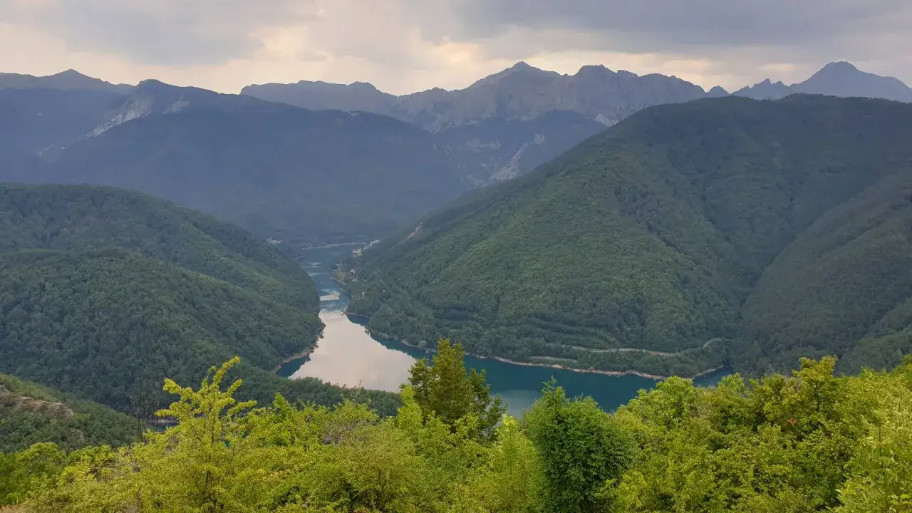 Garfagnana cosa vedere: un lago turchese serpeggia tra montagne boscose, con cime rocciose all'orizzonte.