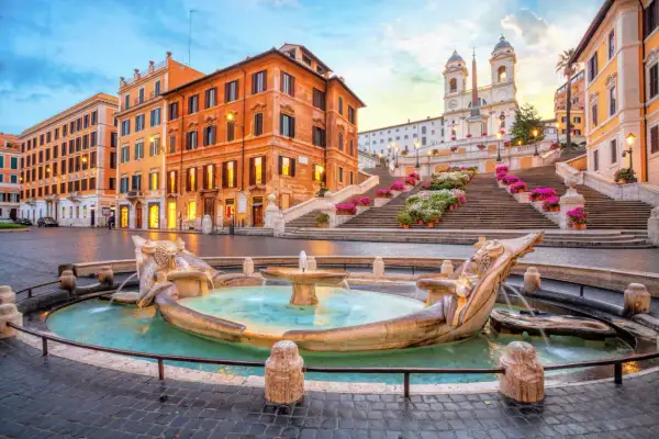 Fontana della Barcaccia e scalinata di Trinità dei Monti a Roma, con edifici storici e fiori colorati.